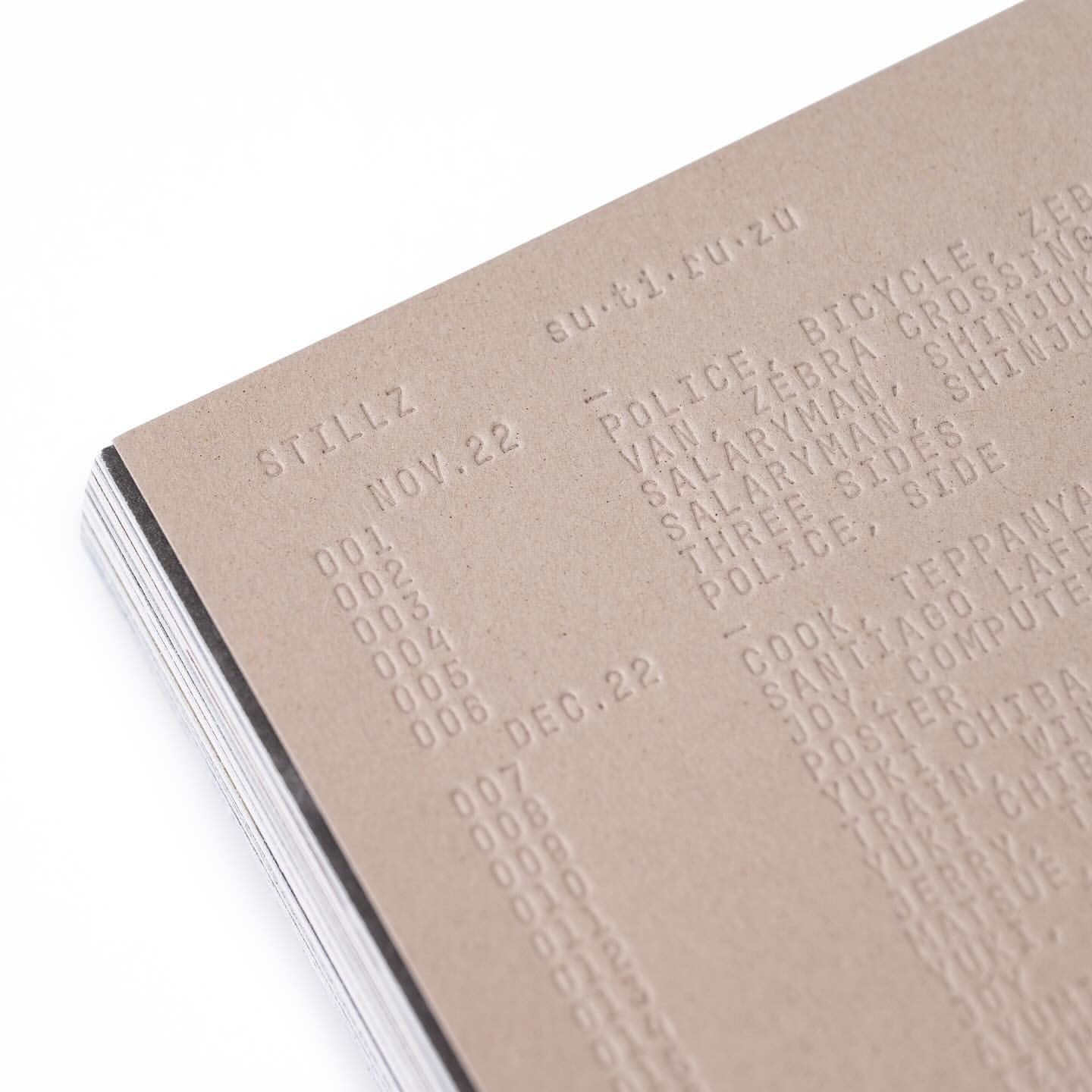 Close-up of a stack of paper with text embossed on the top sheet, featuring dates, titles, and locations in a textured, monochromatic composition.