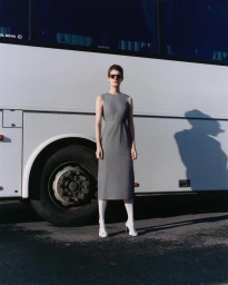 Model in grey midi dress and sunglasses standing before a white bus wheel