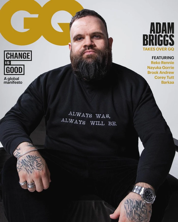 Portrait of Adam Briggs with a full beard wearing a black sweatshirt with text against a white background