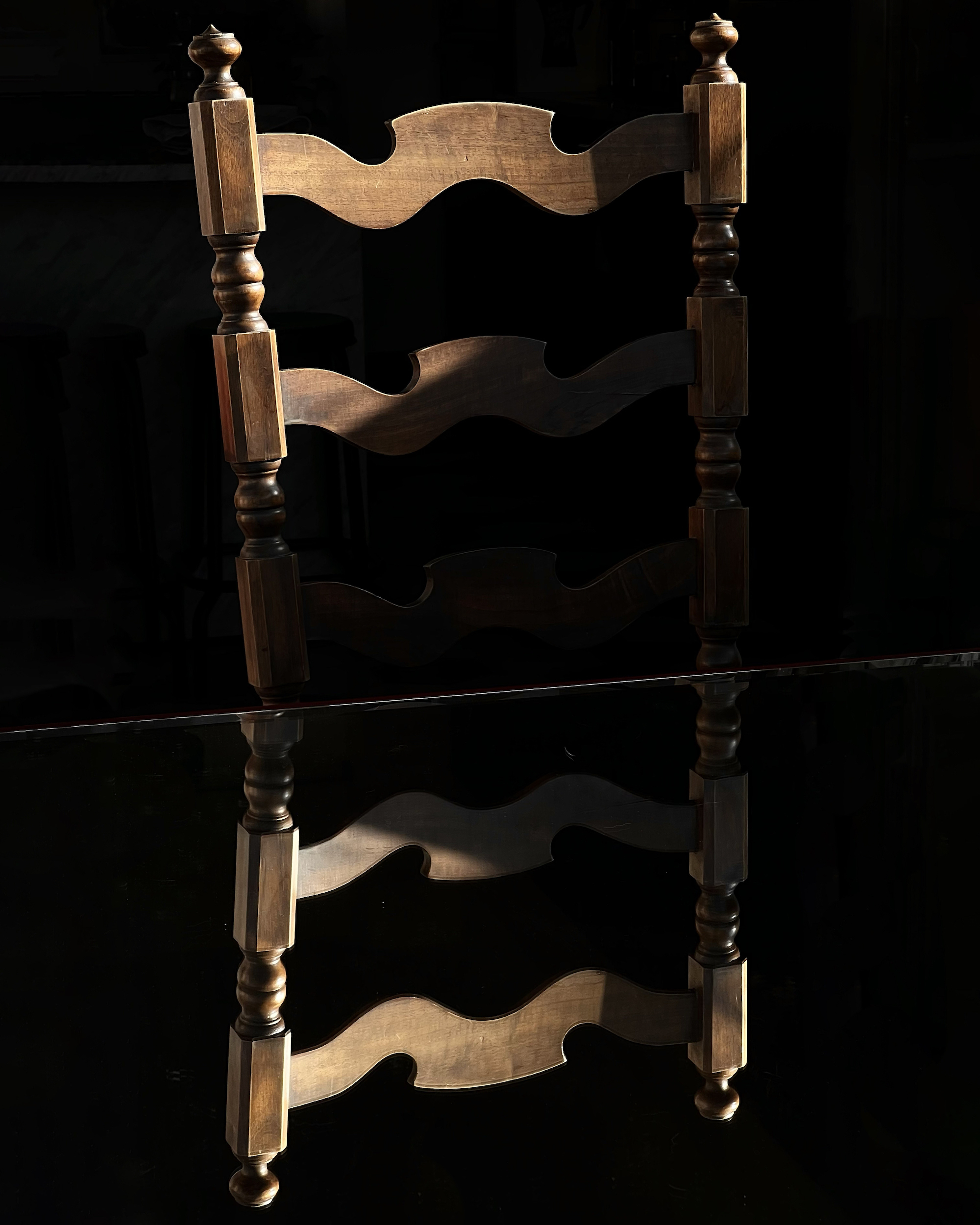 Wooden chair lit by a direct light beam against a black background with a dark surface reflection