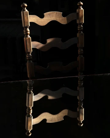 Wooden chair lit by a direct light beam against a black background with a dark surface reflection