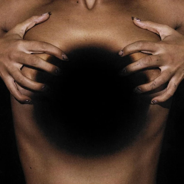 Close-up studio shot of a fair-skinned adult female holding her breasts, showcasing manicure details and dramatic lighting.