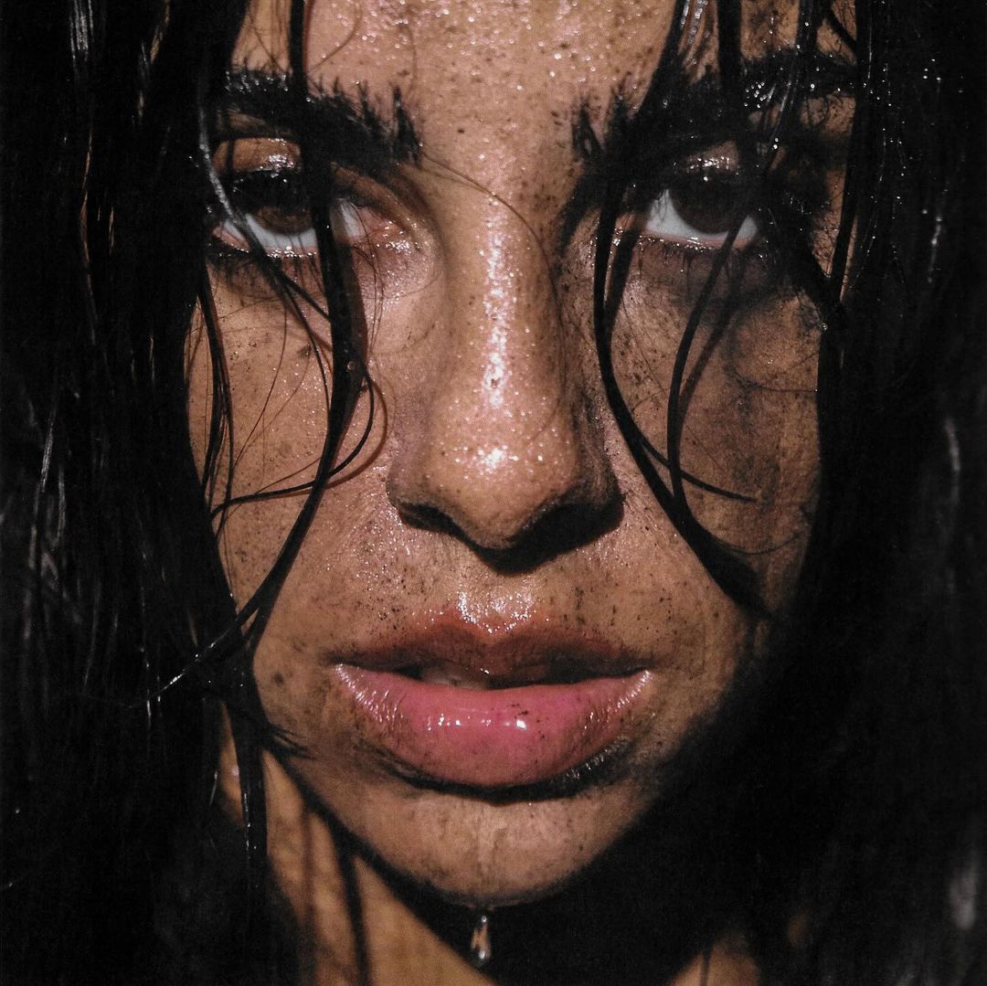 Close-up portrait of a person with wet, dark hair and a slightly dirty face looking directly at the camera with a neutral expression.