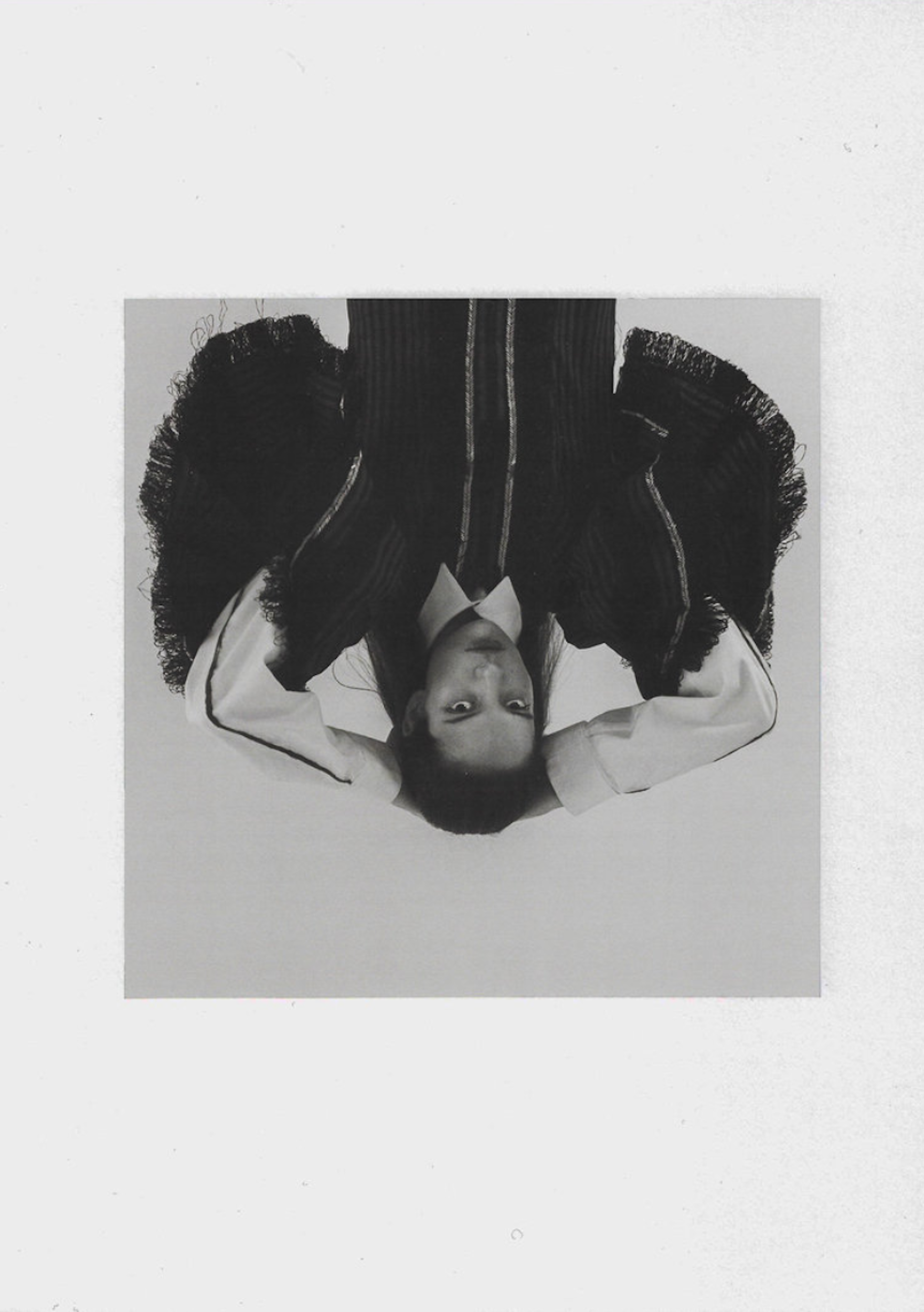 Monochrome portrait of a person in a collared shirt and dark blazer, positioned upside down against a white background.