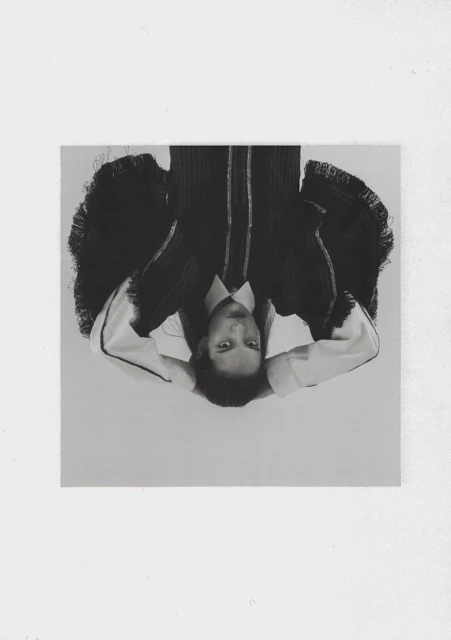 Monochrome portrait of a person in a collared shirt and dark blazer, positioned upside down against a white background.