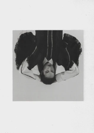 Monochrome portrait of a person in a collared shirt and dark blazer, positioned upside down against a white background.