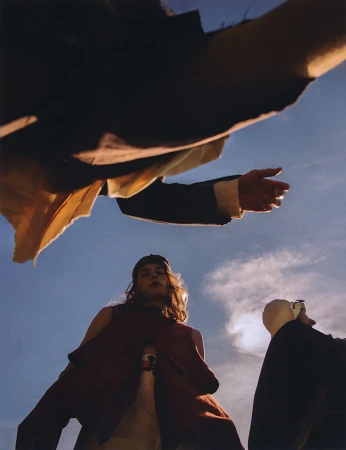 Low angle worm's-eye view of a model in a red sleeveless tunic against a bright blue sky with clouds.