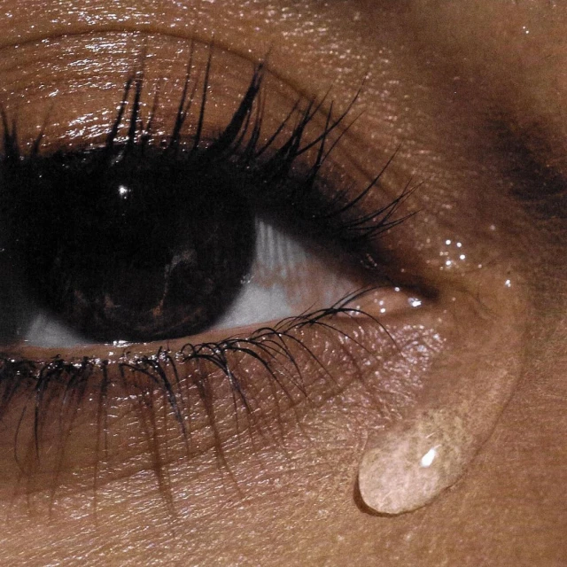 Close-up of a woman's eye with long, dark eyelashes and a single tear rolling down her cheek, captured with a shallow depth of field.