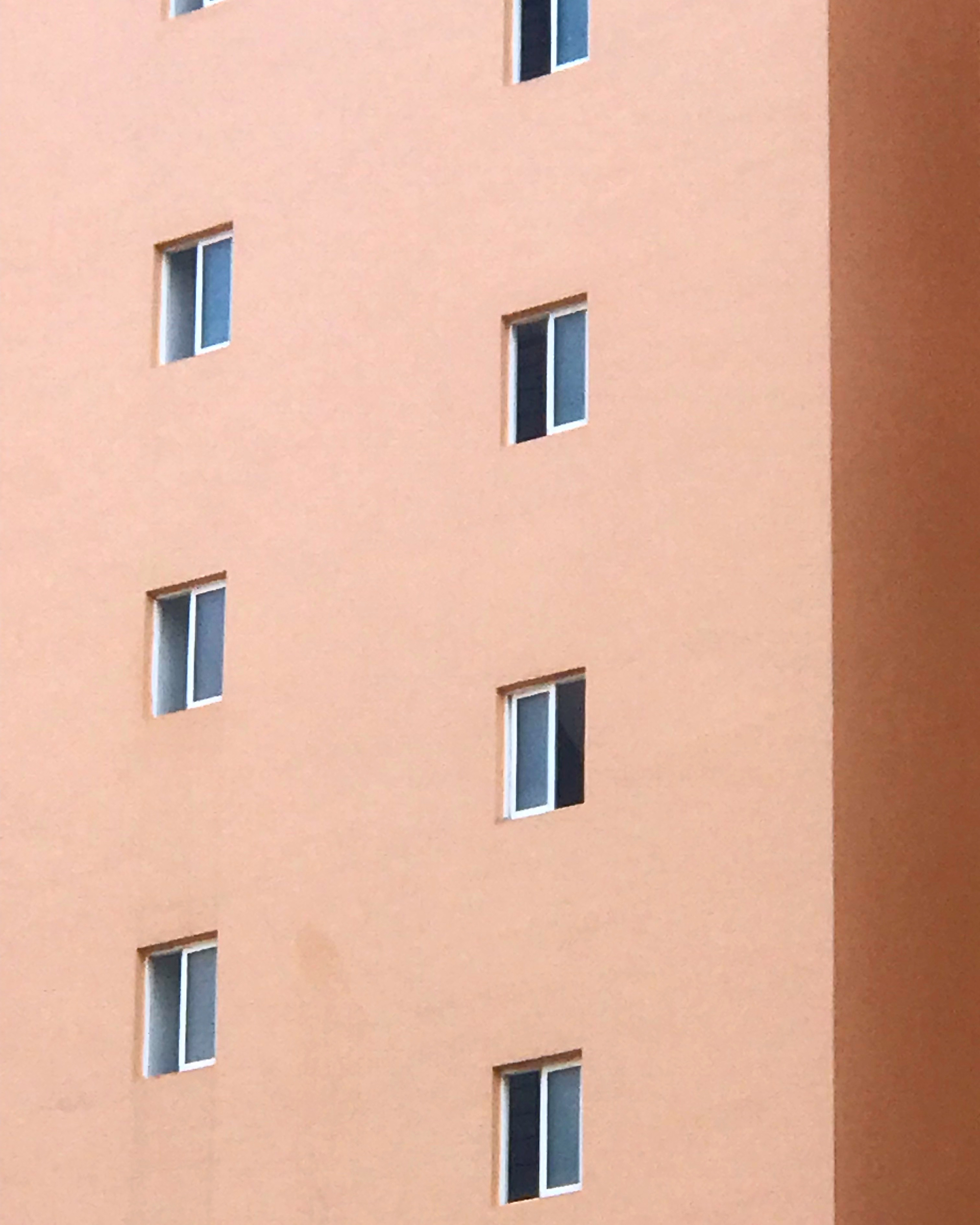 Close-up of a peach building exterior featuring rows of windows with white frames and blue tinted glass, creating a pattern.