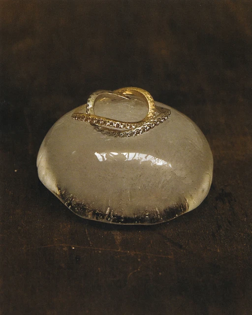 Close-up of a gold ring with embedded stones resting on a smooth, light gray stone against a dark brown background.