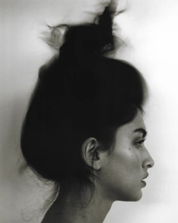 Profile portrait of a woman with dark hair in a high updo against a plain white background by Adriana Roslin