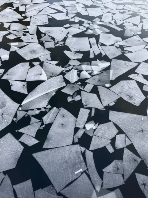 An aerial view of dark water with white ice fragments in a variety of shapes and sizes floating on the surface.