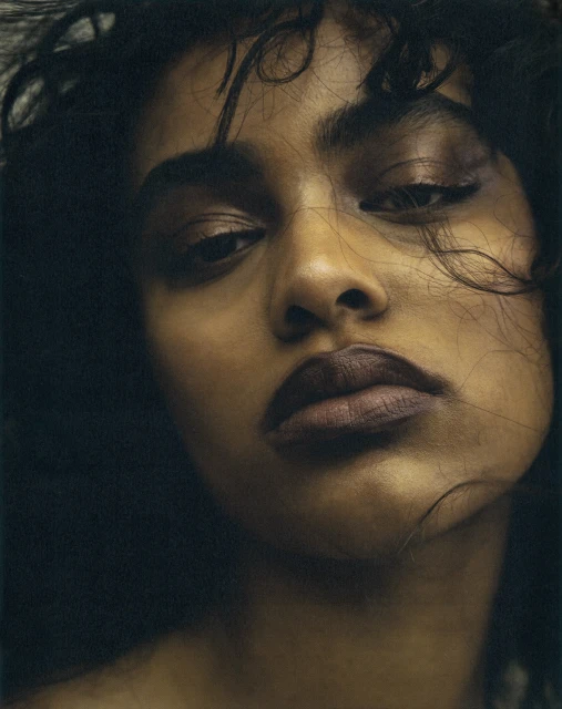 Close-up portrait of a dark-skinned woman with curly hair, focusing on her face and makeup, shot in a studio environment.
