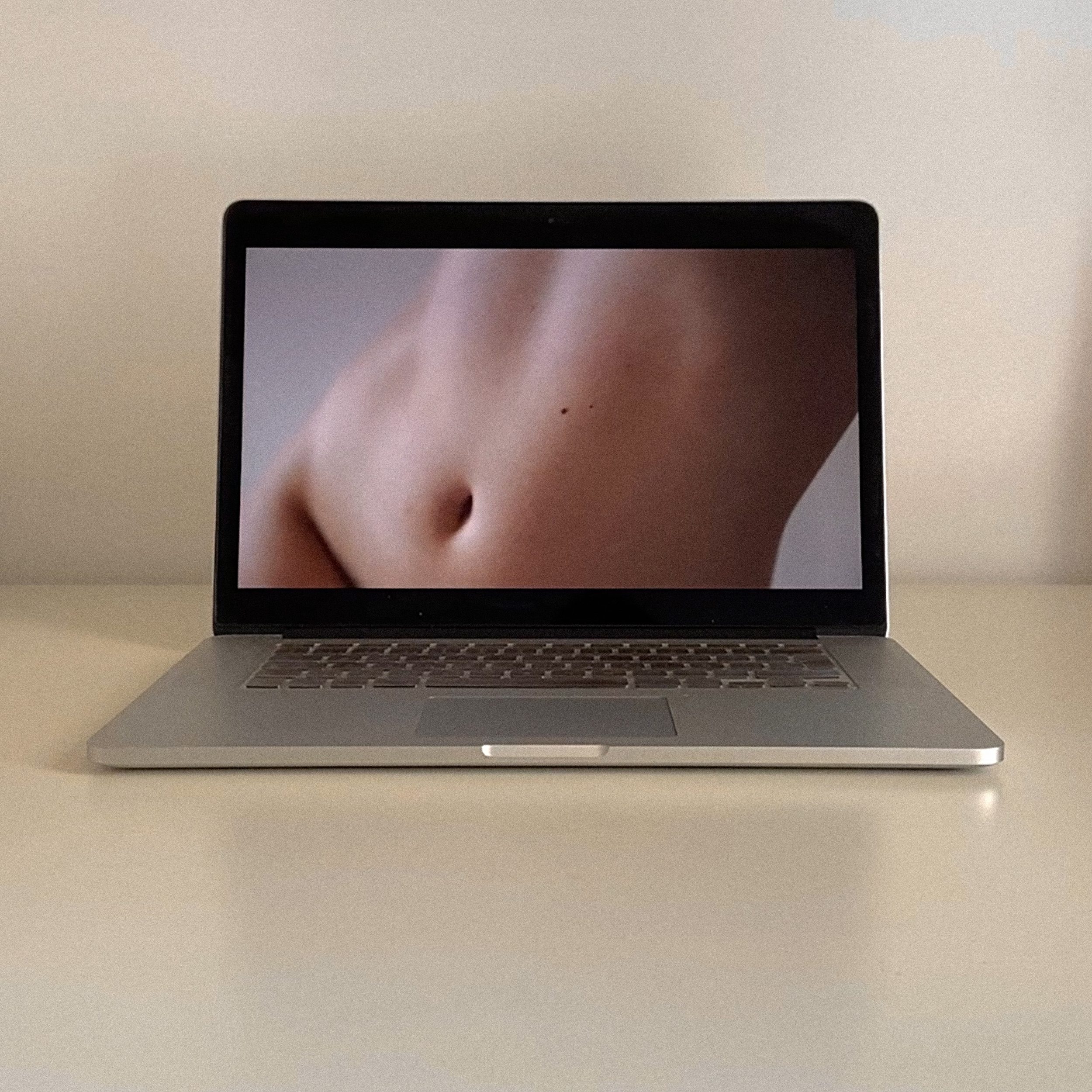 Laptop computer displays a close-up image of a bare abdomen against a neutral background indoors with bright, soft lighting.