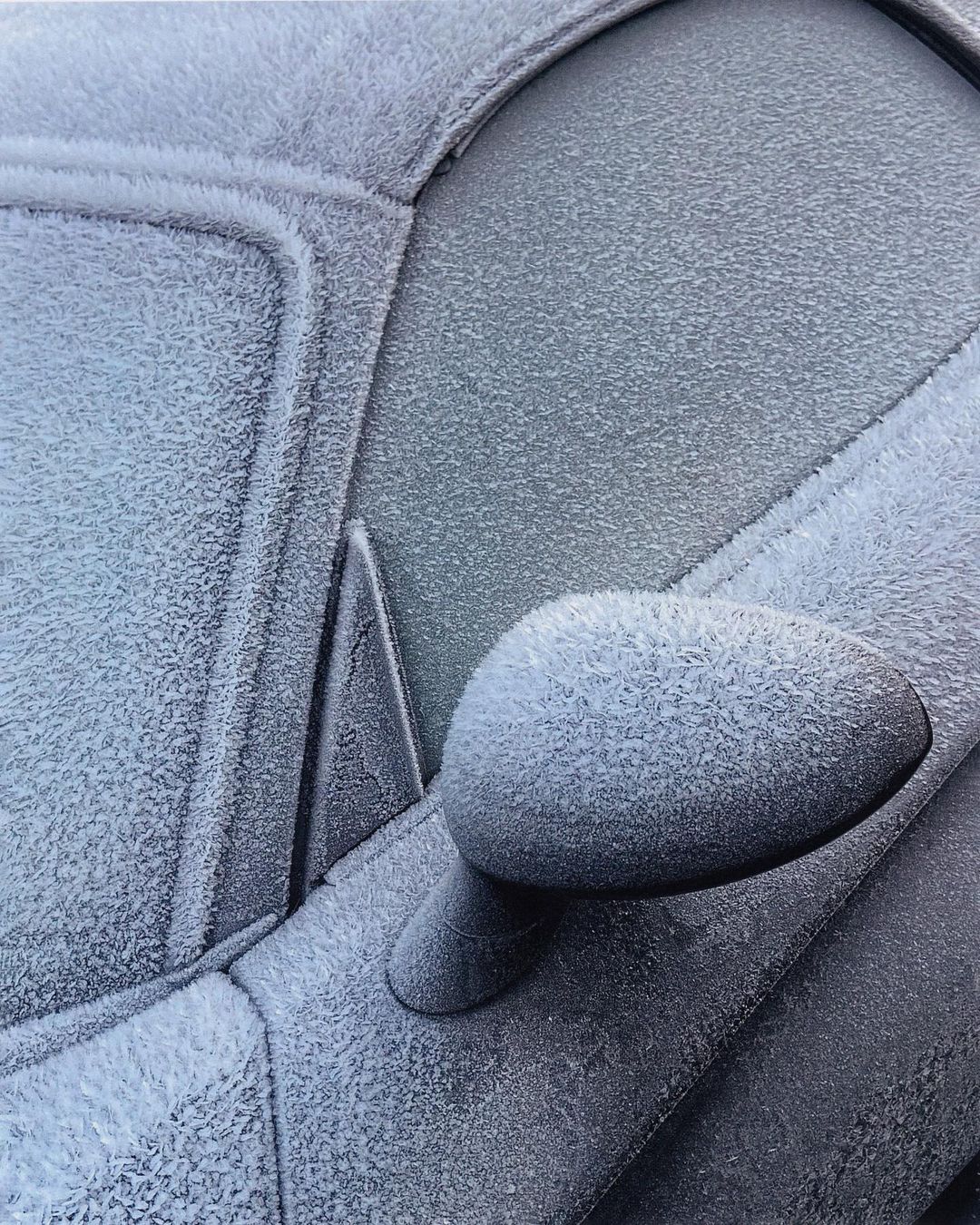 Close-up of a vehicle covered in frost and ice crystals, showcasing intricate patterns formed by frozen condensation on a cold day.
