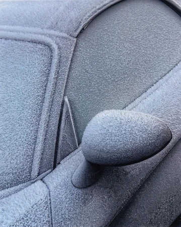 Close-up of a vehicle covered in frost and ice crystals, showcasing intricate patterns formed by frozen condensation on a cold day.
