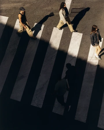 Aerial view of three people in casual outfits crossing a pedestrian crosswalk with zebra stripes on an asphalt road on a sunny day.