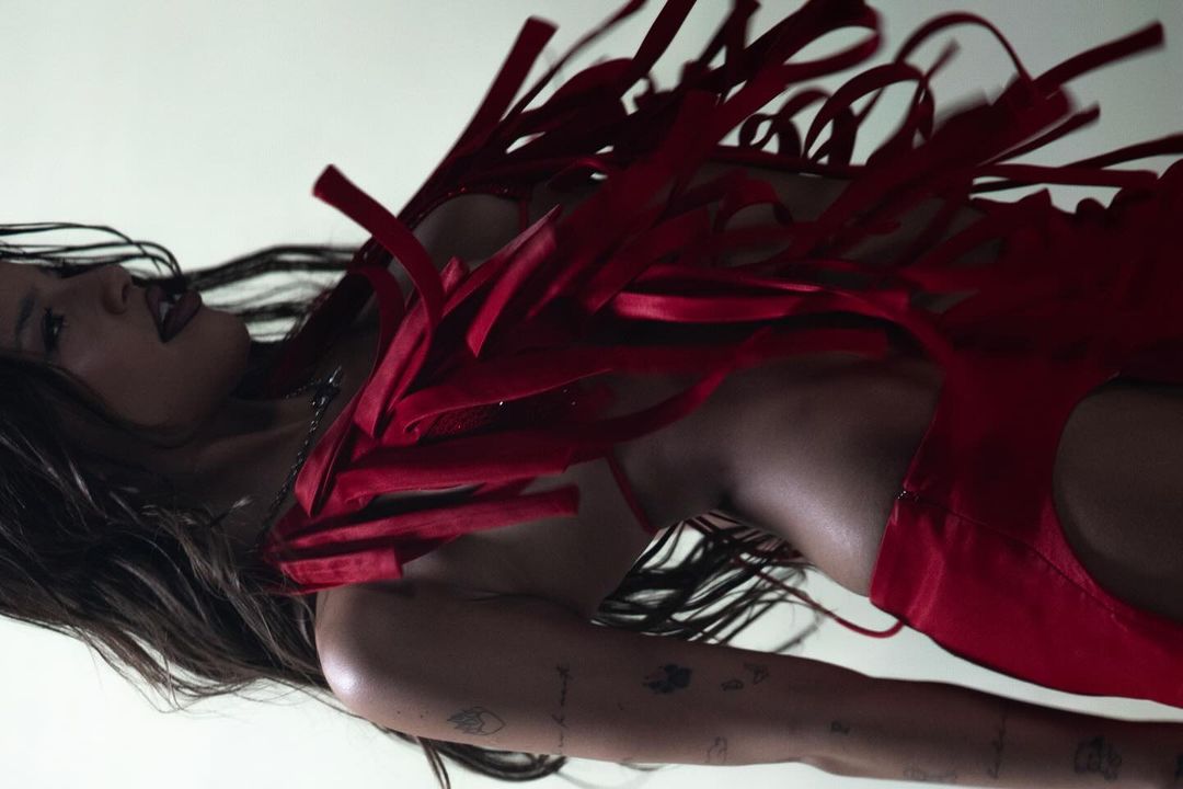 Adult woman in red dress with fringe detail, posing indoors under bright lighting, showcasing fashion and beauty elements. 