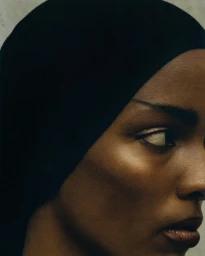 Close-up portrait of a black woman wearing a black head covering against a neutral textured background, photographed by Adriana Roslin.
