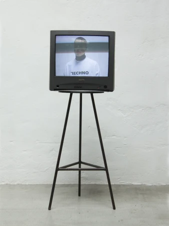 Vintage television on a metal stand displays a person wearing a white shirt with 'Techno' text in a minimalist setting.