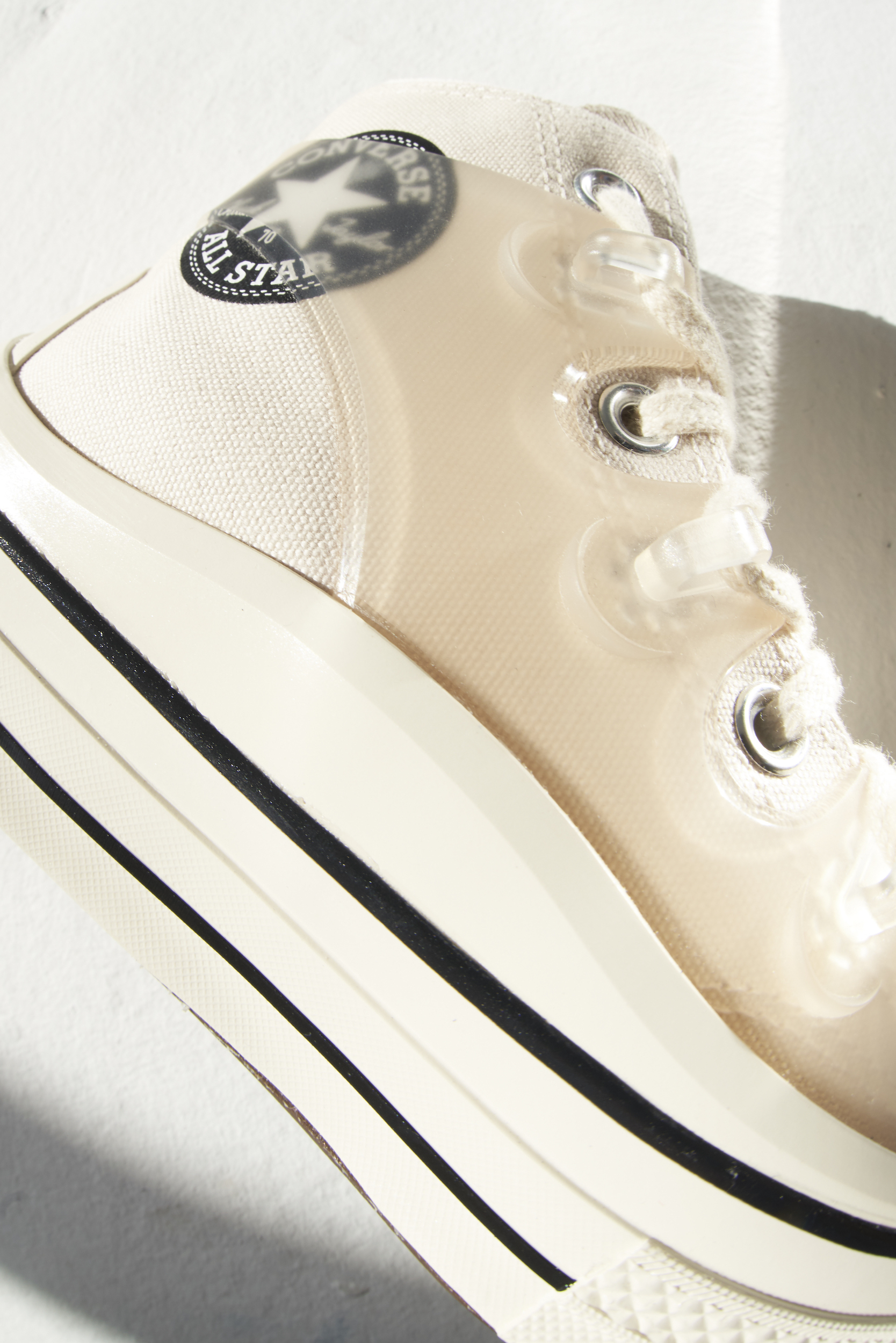 Close-up studio shot of a translucent and white Converse All Star sneaker featuring a star logo and striped platform sole.