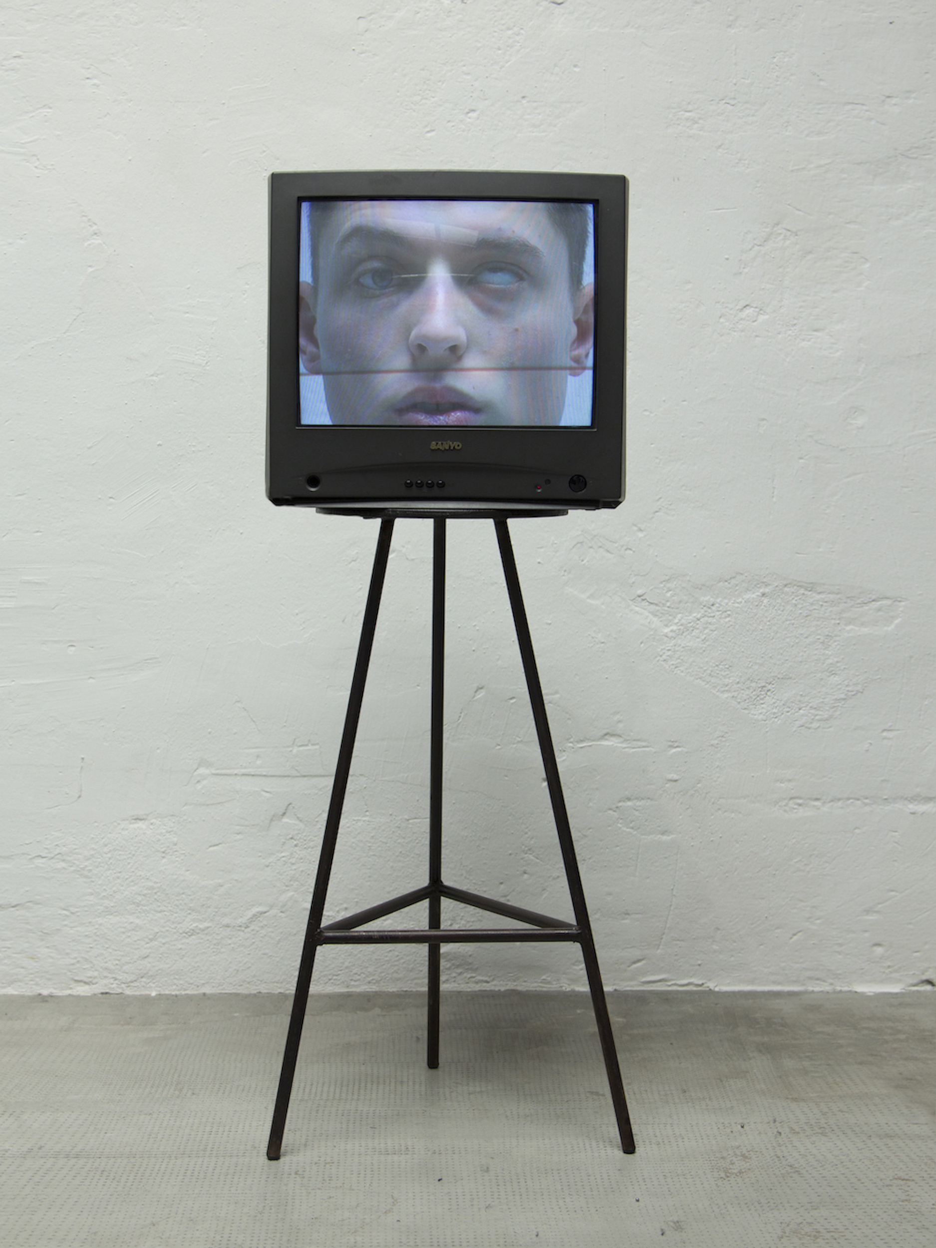 A vintage CRT television displays a man's face on a stand against a white textured wall indoors, highlighting digital art and technology.