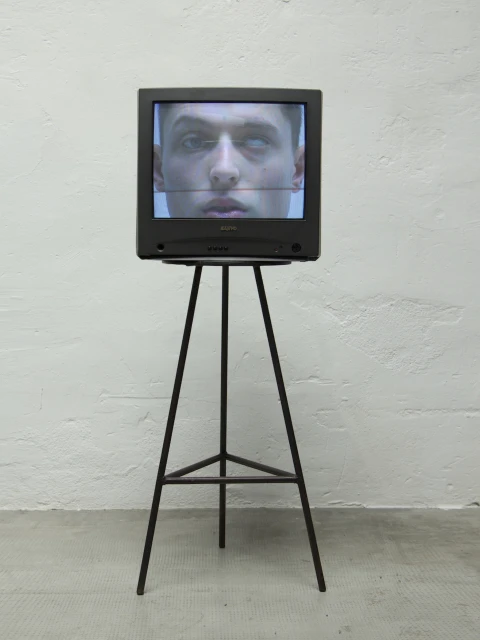 A vintage CRT television displays a man's face on a stand against a white textured wall indoors, highlighting digital art and technology.