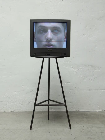 A vintage CRT television displays a man's face on a stand against a white textured wall indoors, highlighting digital art and technology.