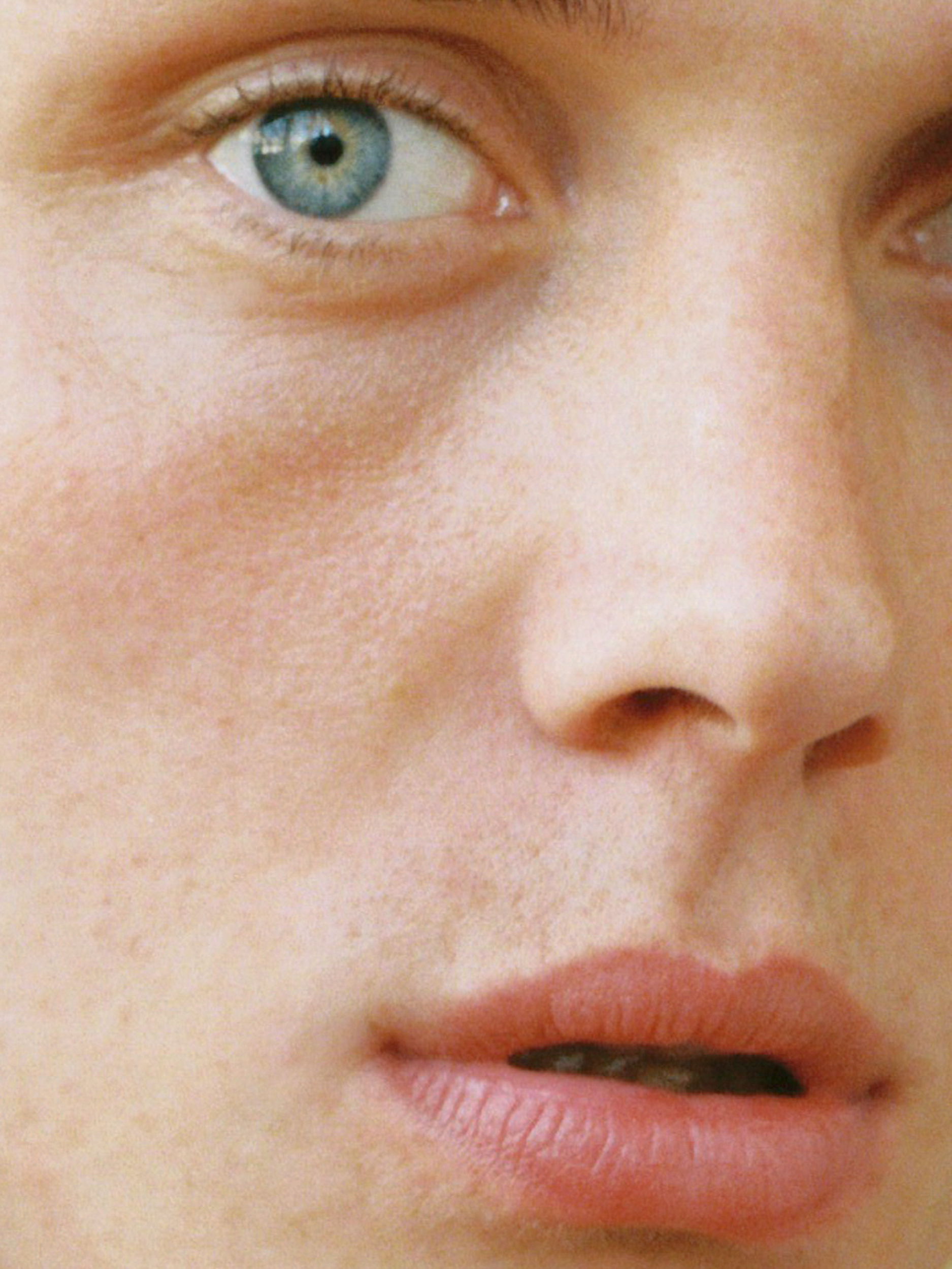 Close-up portrait of a human face featuring a blue eye, nose, and mouth, with soft lighting and focus on facial details and skin texture.
