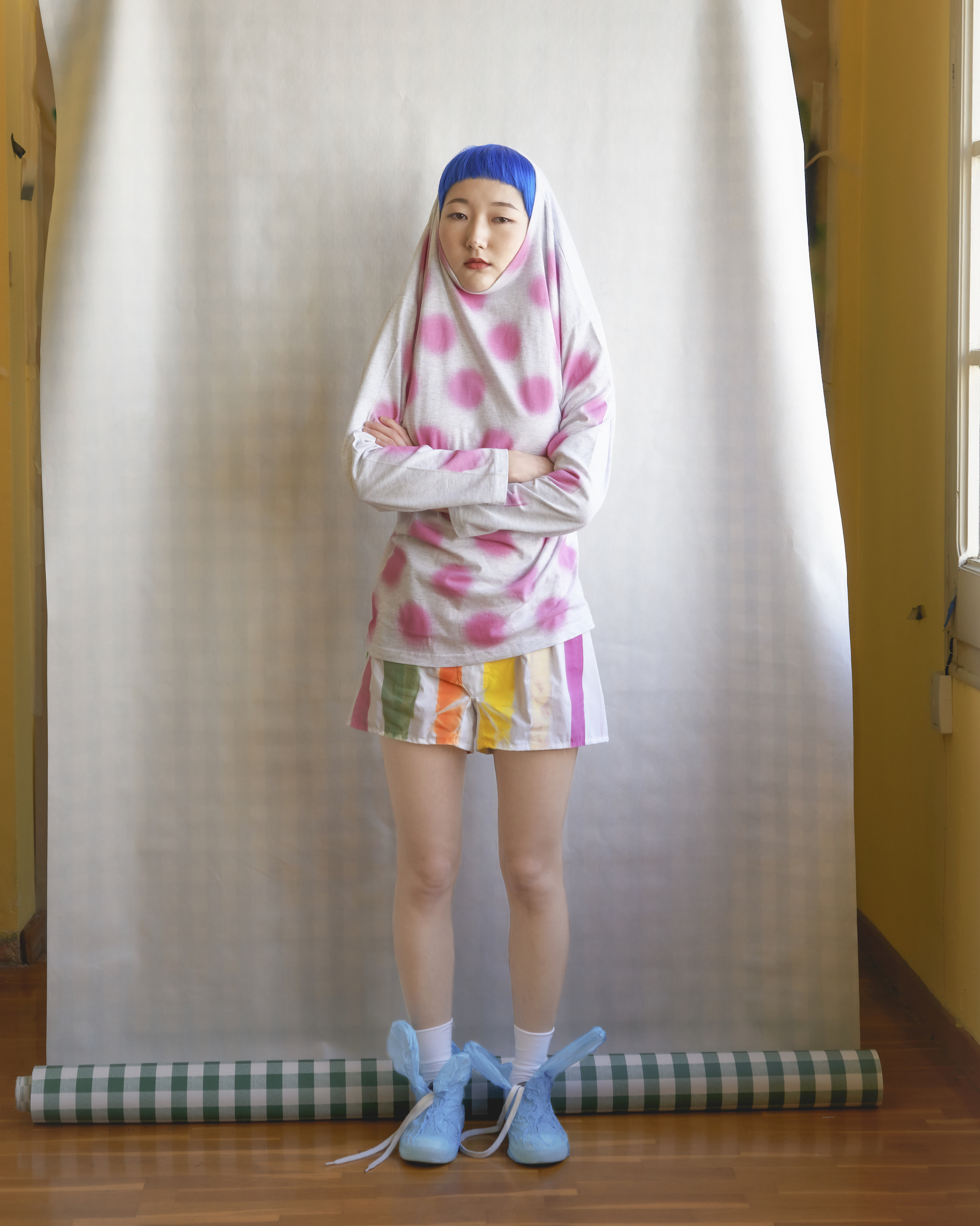 Full-length shot of a person wearing colorful patterned clothing with blue hair and matching shoes, posing in front of a white backdrop.