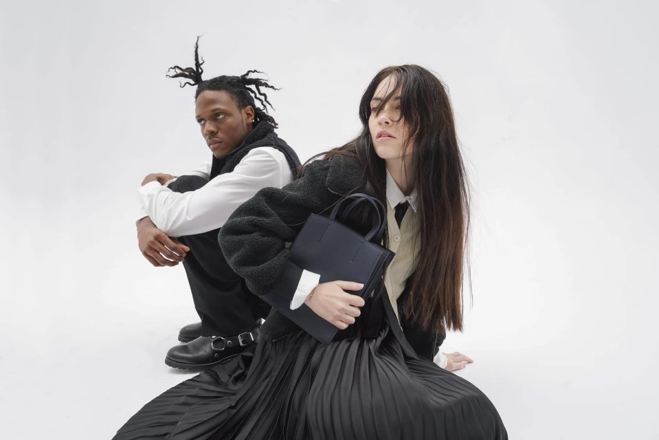 Two models pose on a white background. One holds a black tote bag. Both are wearing black and white business casual attire.