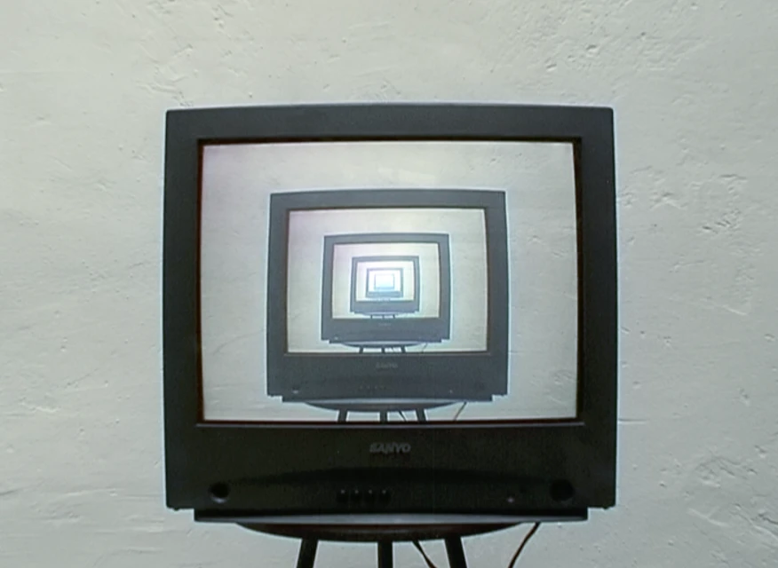 A black cathode-ray television on a stand shows a recursive screen display, diminishing into the distance, against a white wall.