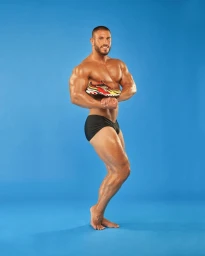 Muscular man posing against a blue seamless background holding a colourful sports sneaker against his chest