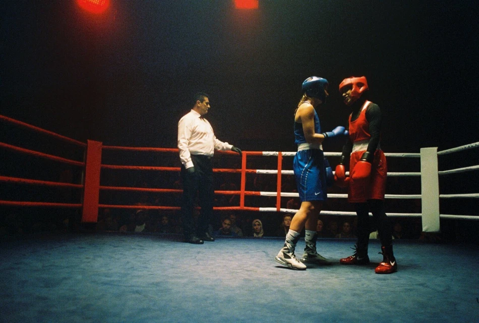 Two boxers face off in the boxing ring as the referee stands nearby, the crowd can be seen blurred in the background.