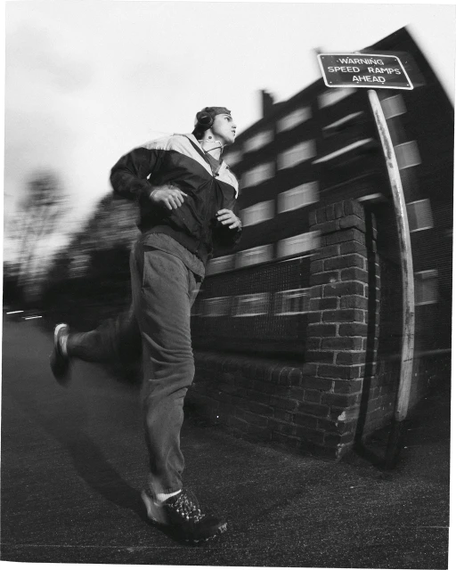 Monochrome action shot of a man running past a speed ramps sign and brick wall with motion blur.