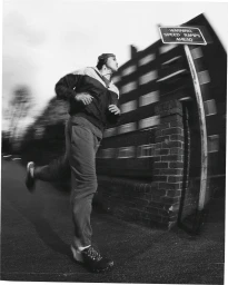 Monochrome action shot of a man running past a speed ramps sign and brick wall with motion blur.