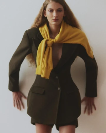 Model wearing a dark blazer and a yellow sweater tied around shoulders against a plain background by Cecilia Duarte.