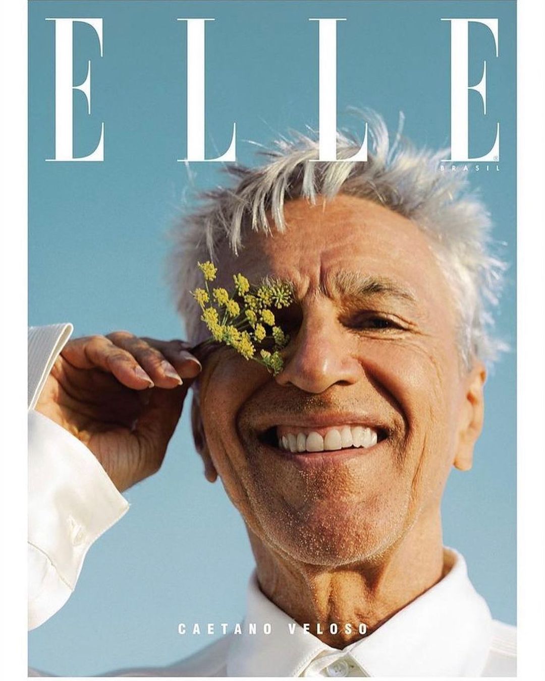 Elle magazine cover featuring an elderly man, Caetano Veloso, posing with a small yellow flower covering one eye, set against a blue sky backdrop.