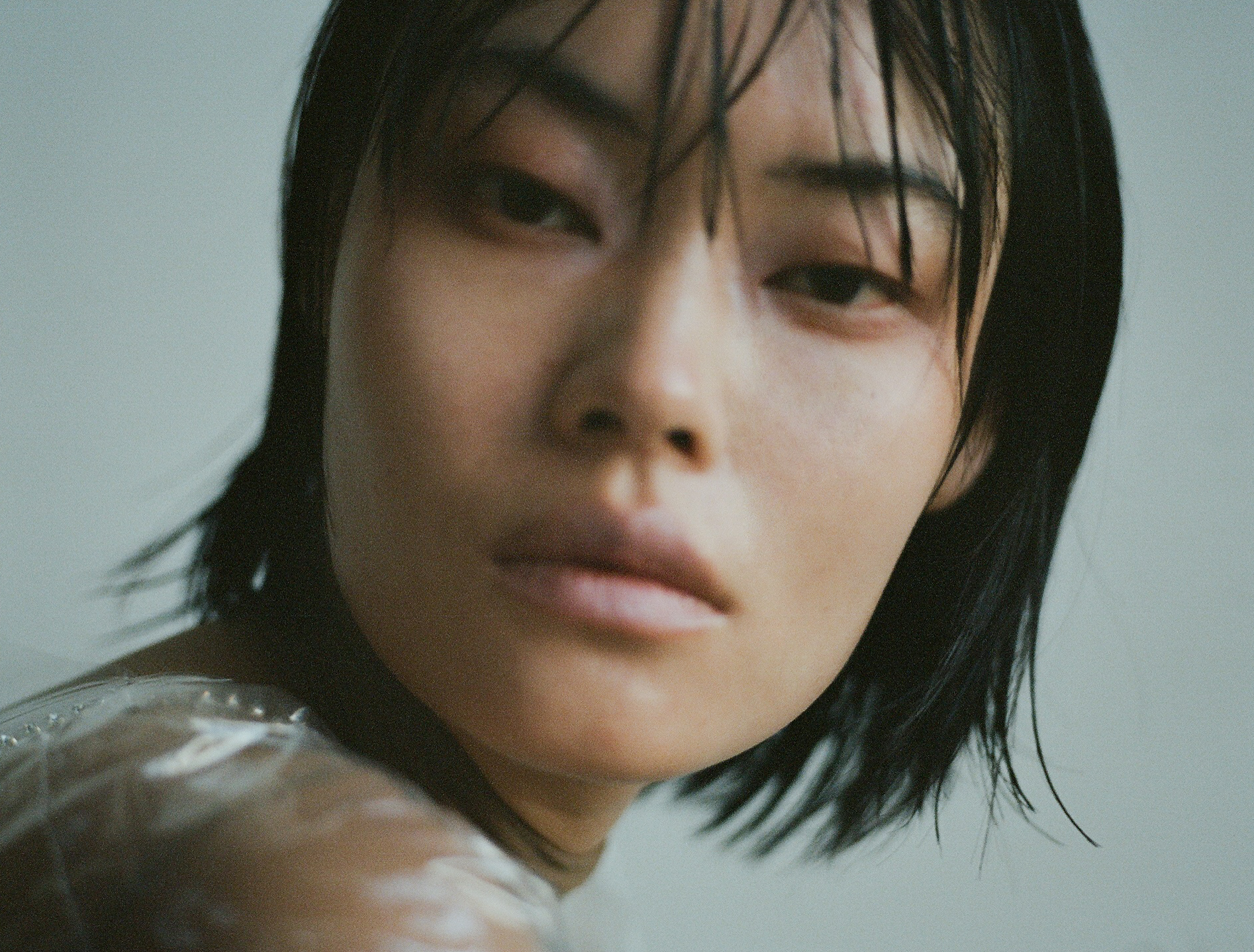 Close-up portrait of an East Asian woman with wet dark hair and direct gaze against a neutral background.