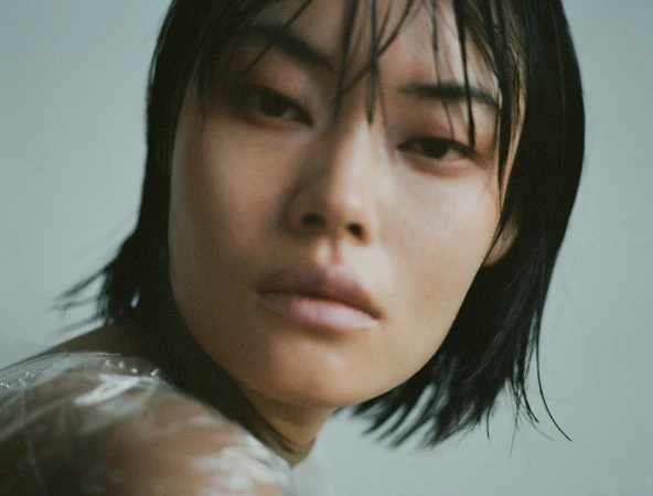 Close-up portrait of an East Asian woman with wet dark hair and direct gaze against a neutral background.