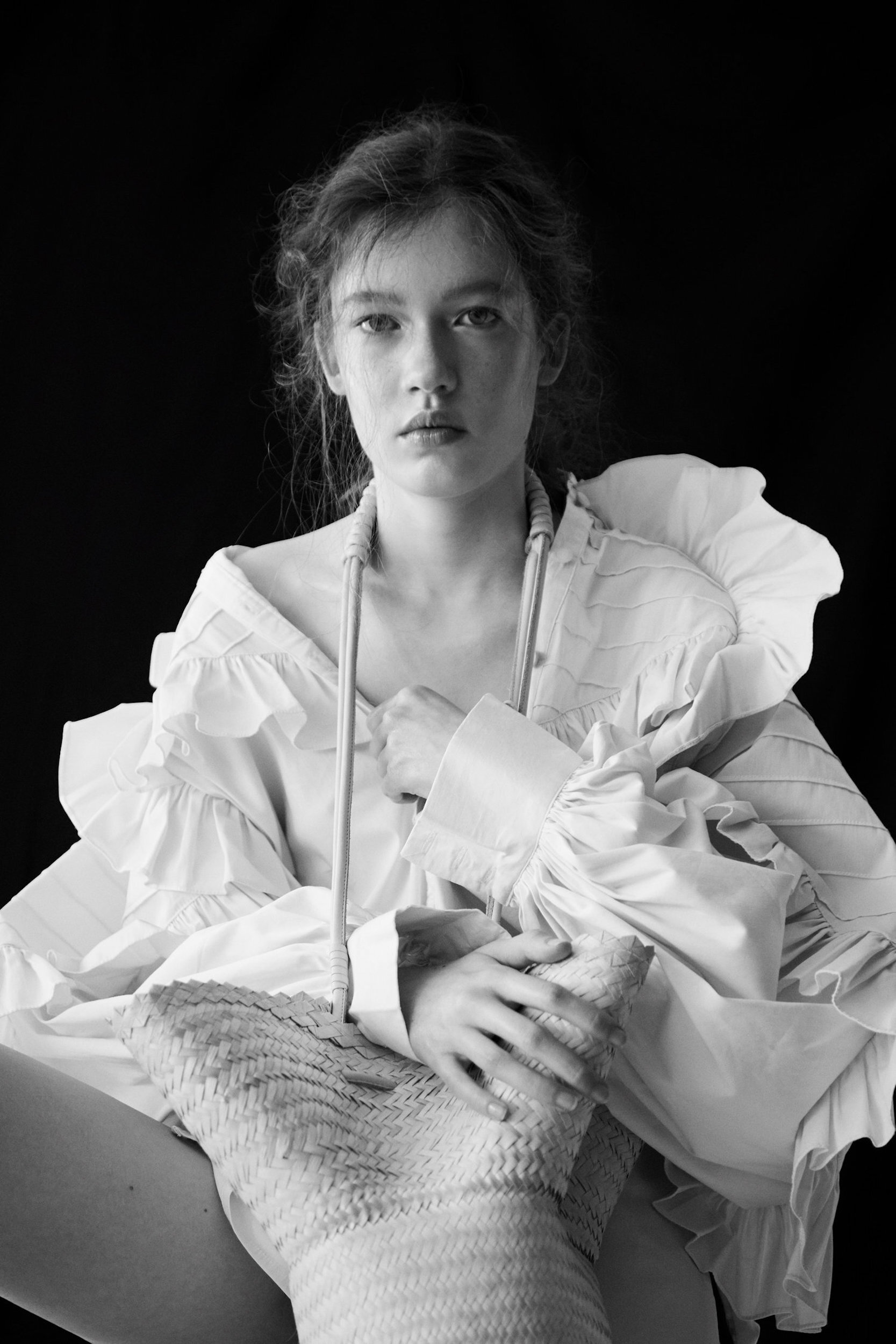 Monochrome portrait of a young adult female model wearing a white ruffle shirt, against a dark background. The model has fair skin.