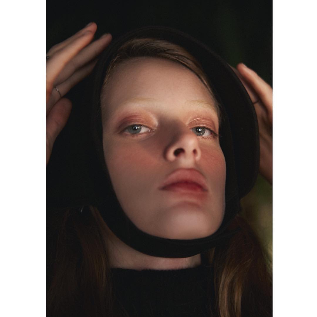 Close-up portrait of a young fair-skinned woman with blue eyes wearing a black head covering and top, illuminated against a dark background.