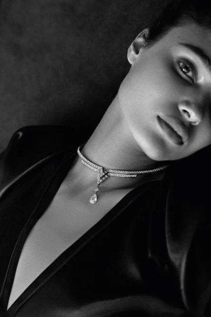 Monochrome portrait of a woman wearing a black top and a delicate diamond choker necklace against a dark grey backdrop.