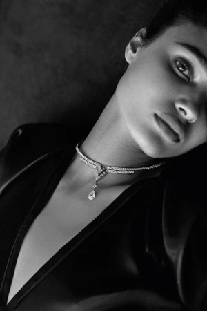 Monochrome portrait of a woman wearing a black top and a delicate diamond choker necklace against a dark grey backdrop.