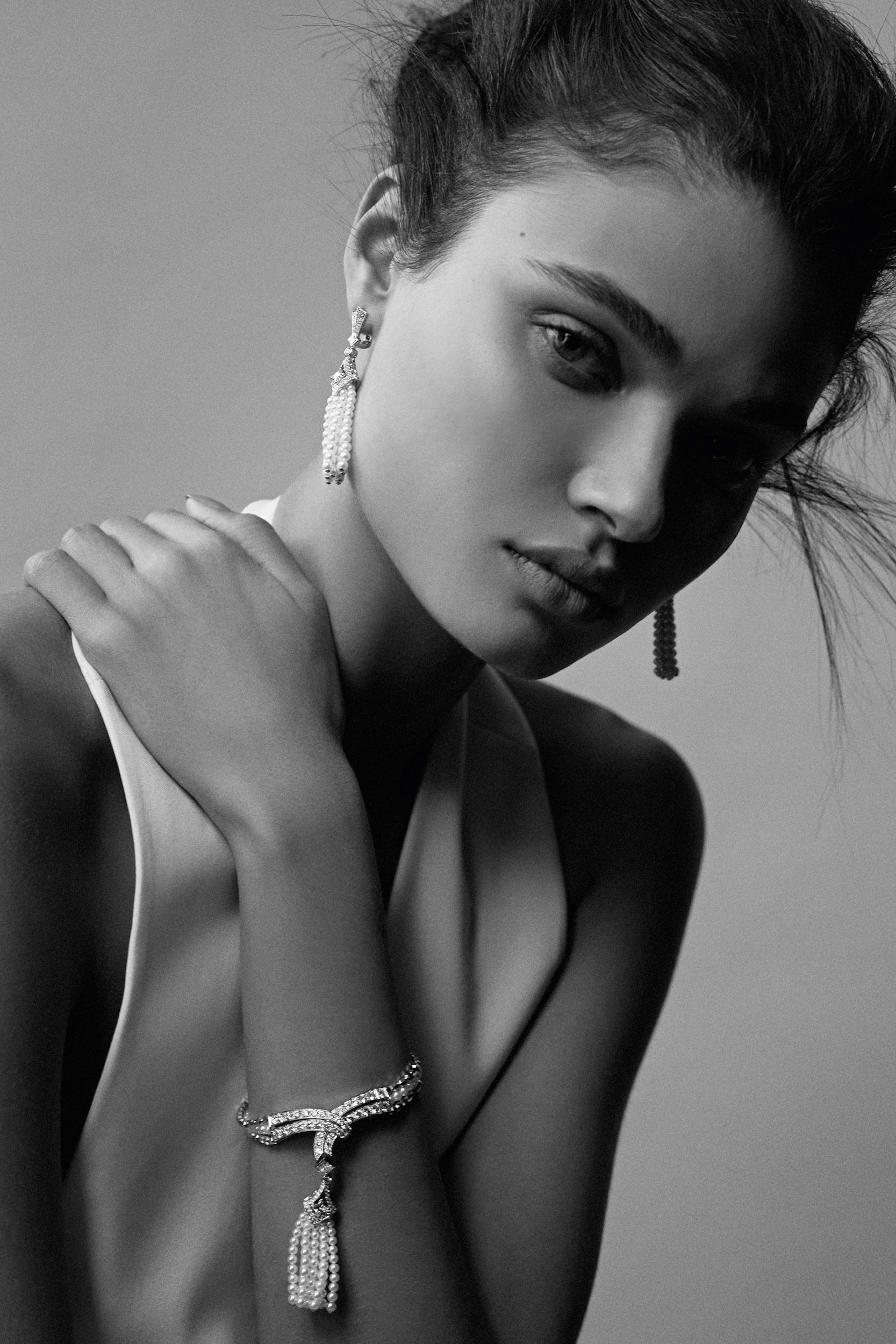 Black and white portrait of a woman wearing jewelry including a bracelet and earrings in a studio with a neutral backdrop.