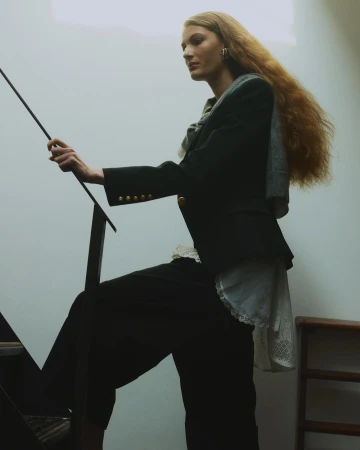 A fair-skinned woman with long wavy hair is ascending stairs while holding onto a black metal railing. She is wearing a dark blazer and pants.