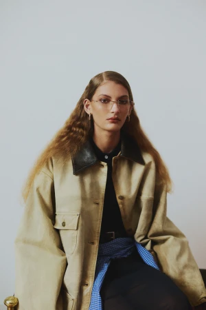 Portrait of a woman with long wavy hair wearing glasses, a beige jacket with a dark collar, and a blue patterned scarf.