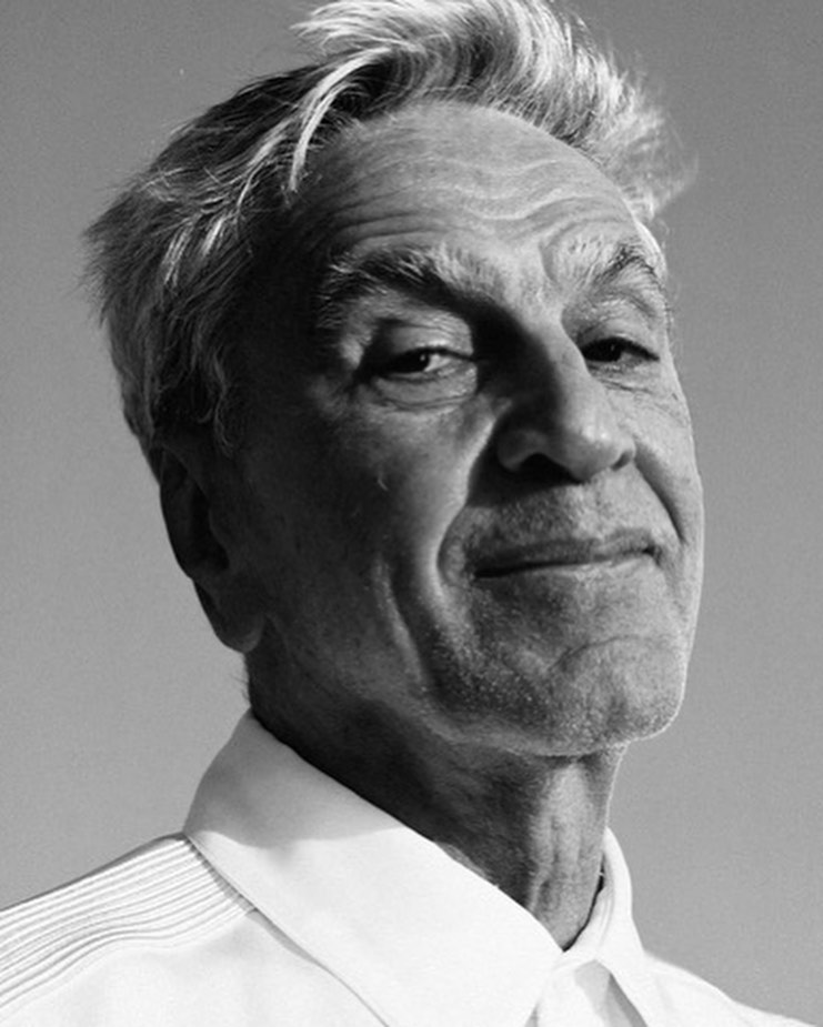 Monochrome portrait of an elderly man with short styled hair wearing a white collared shirt against a clear sky.