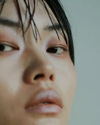 Close-up portrait of a model with wet dark hair and muted eye makeup photographed by Cecilia Duarte.