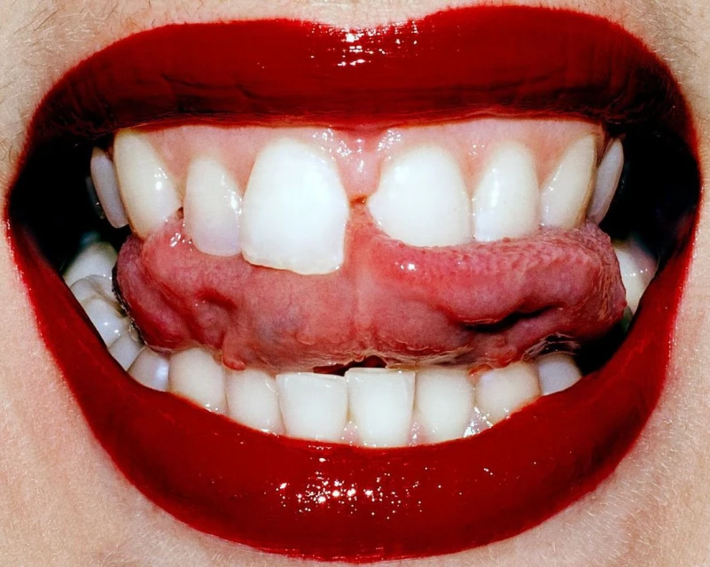 Macro shot featuring bright red lipstick, white teeth and a human tongue. Close-up of a person's mouth, teeth, and tongue with red lipstick.
